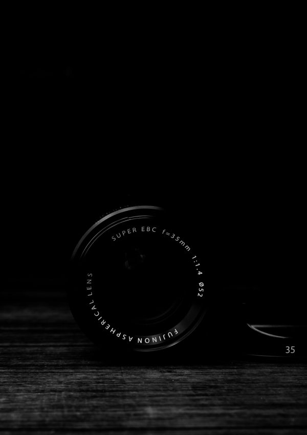 vertical-gray-scale-shot-camera-lens-wooden-surface