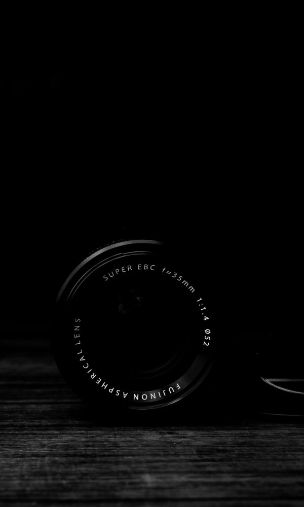 vertical-gray-scale-shot-camera-lens-wooden-surface